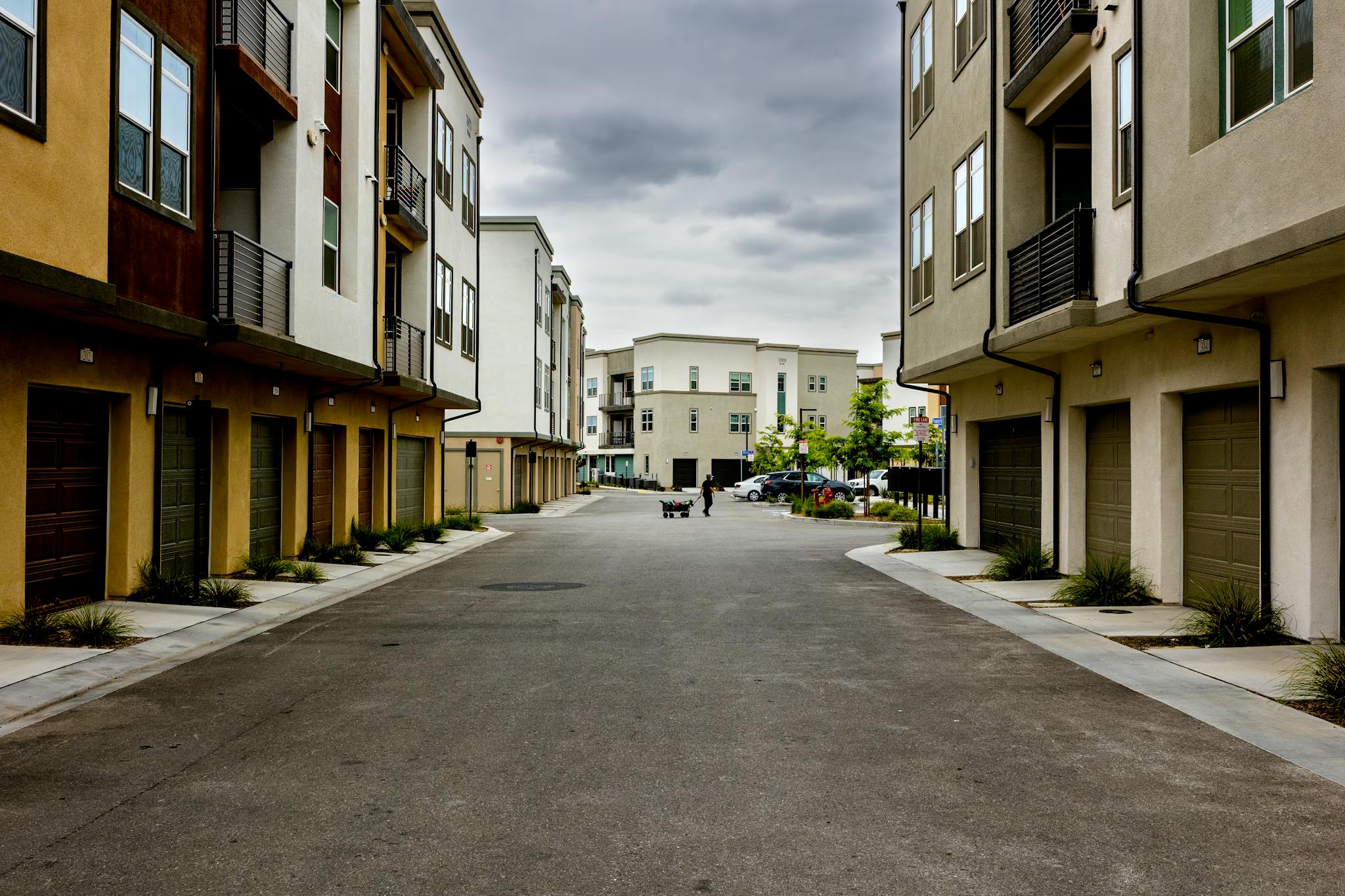 A man pulls a cart down a quiet residential street lined with modern townhouses.